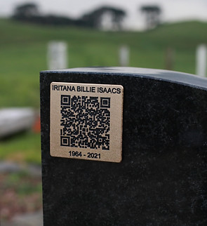 A brass QR code plaque mounted on a headstone